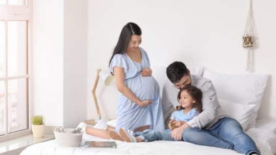 Happy man laying on bed with his daughter and pregnant wife at home